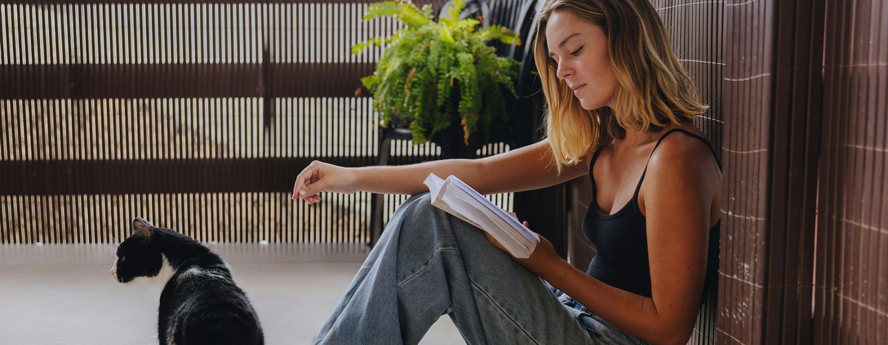A woman sitting on a patio reading with her cat.